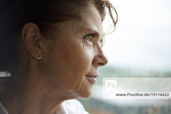 Smiling woman looking through window while standing at home