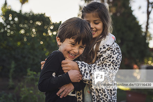 Glückliche Geschwister spielen  während sie bei Sonnenuntergang im Hof stehen
