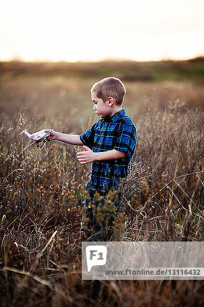 Boy playing with toy while standing on field with plants against sky