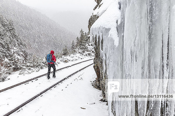 Rückansicht einer Frau die während des Schneefalls in den White Mountains auf einer schneebedeckten Eisenbahnschiene geht