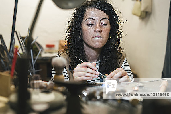 Mitten in einer Werkstatt am Tisch sitzend  in der eine Handwerkerin einen Ring herstellt