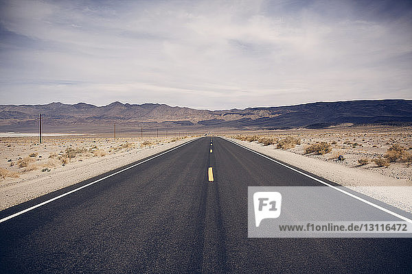 Landstraße  die im Death Valley National Park gegen bewölkten Himmel in Richtung Berge führt