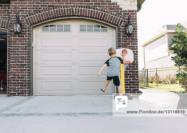 Rear view of boy playing basketball on driveway