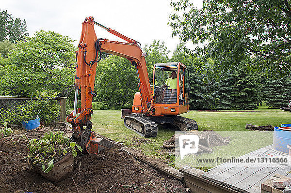Mann in Erdbewegungsmaschine gräbt Erde auf Baustelle