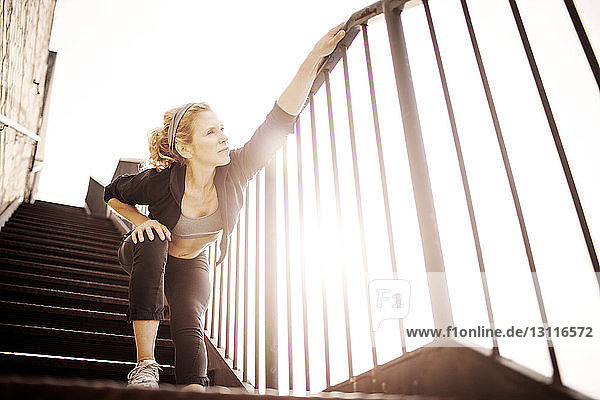 Weibliche Sportlerin trainiert an einem sonnigen Tag auf einer Treppe vor klarem Himmel
