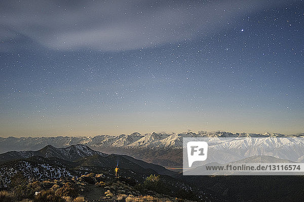 Distant view of hiker standing amidst mountains against star field sky