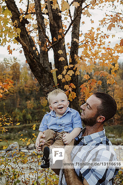 Father carrying son while standing in forest during autumn