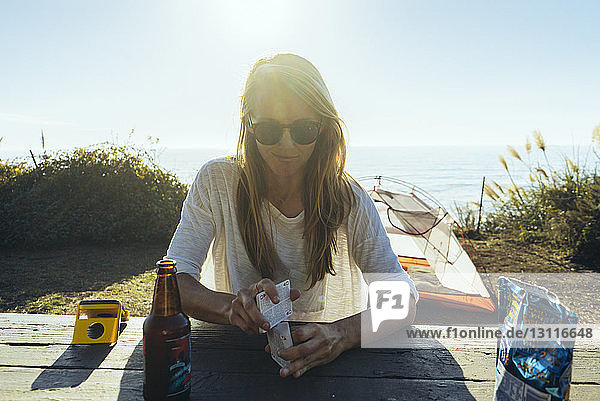 Woman holding cards while sitting at table on field against sea