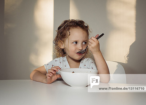 Girl looking away while eating food on table at home