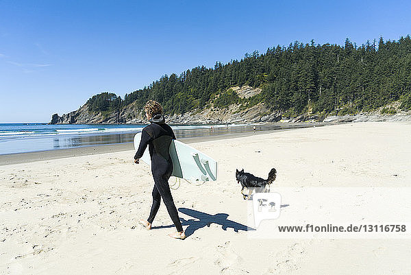 Mann hält Surfbrett mit Hund beim Spaziergang am Strand