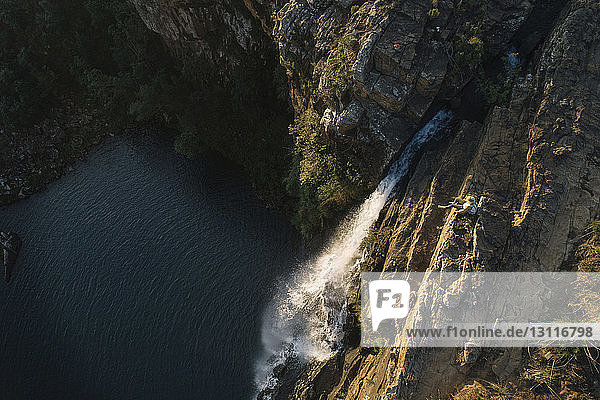 Hochwinkelaufnahme einer Frau  die auf einem Berg am Wasserfall im Wald sitzt