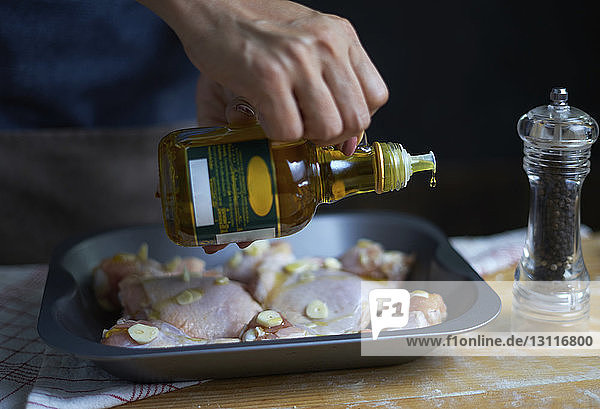 Mitschnitt einer Frau,  die in einem Tablett Olivenöl auf Hühnerfleisch gießt