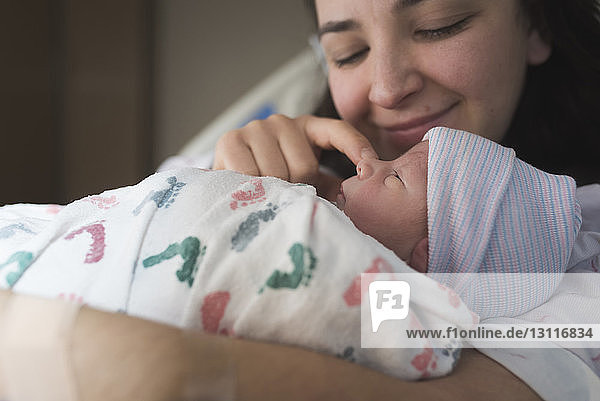 Nahaufnahme einer Mutter  die mit ihrem neugeborenen Sohn spielt  während sie sich im Krankenhaus im Bett ausruht