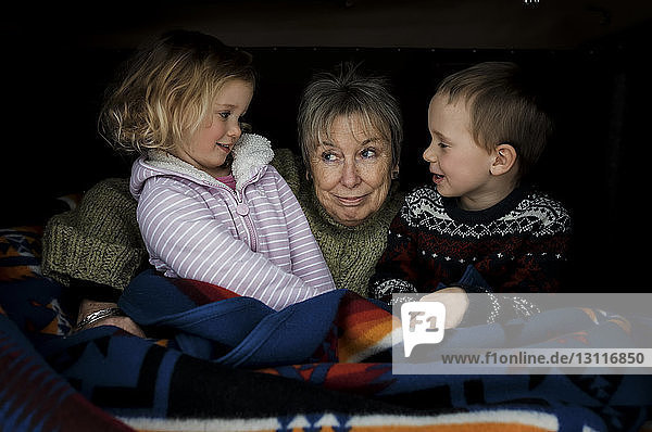 Smiling grandchildren with grandmother sitting in roof tent on car