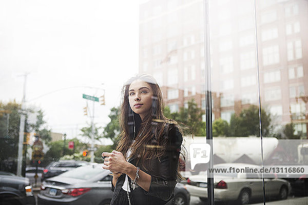 Confident woman standing against cars seen through glass window