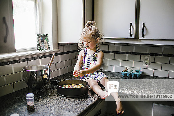 Mädchen bereitet Essen in Behälter vor  während sie auf der Küchentheke sitzt