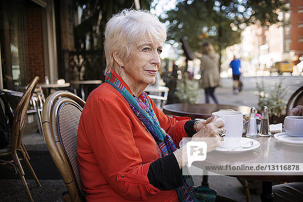 Nachdenkliche ältere Frau hält Kaffeetasse  während sie im Straßencafé sitzt