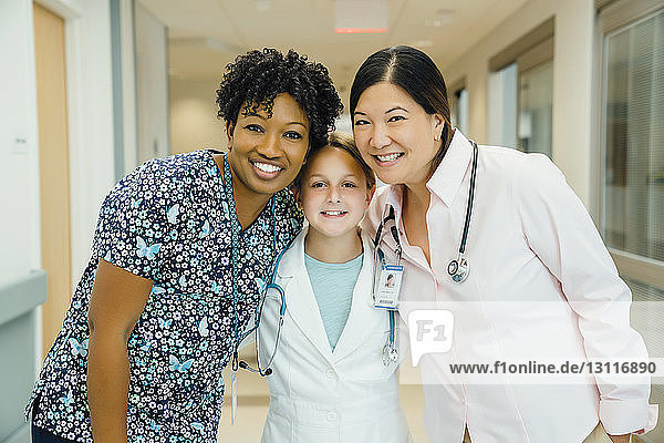 Porträt von selbstbewussten Ärztinnen mit Mädchen im Laborkittel im Krankenhauskorridor