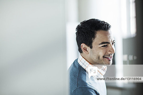 Happy businessman leaning against wall in office