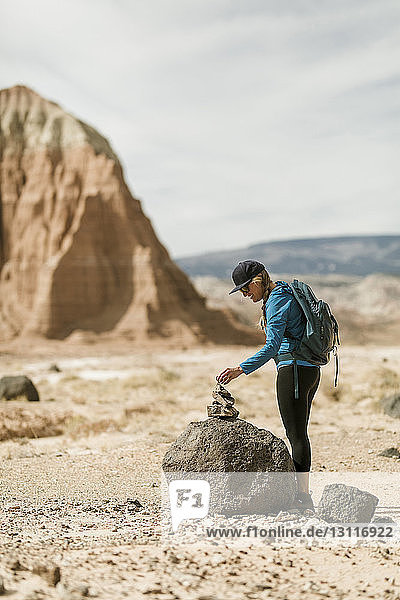 Side view of female hiker stacking rocks while standing at desert