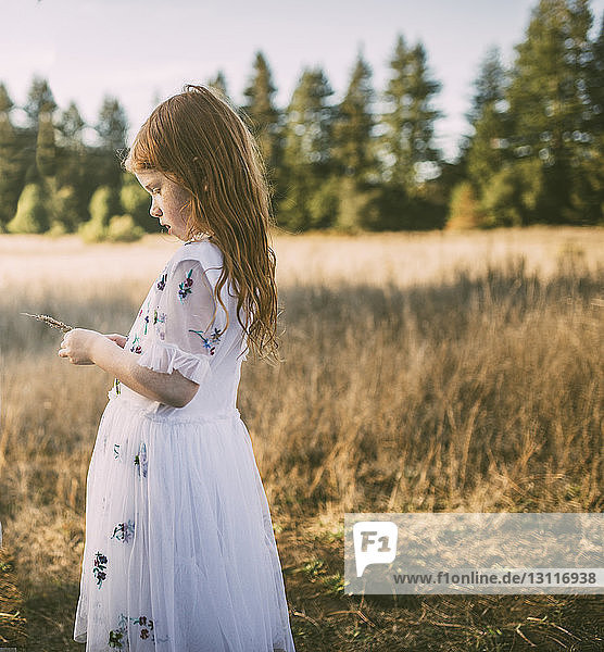 Side view of girl holding plant while standing on field at park
