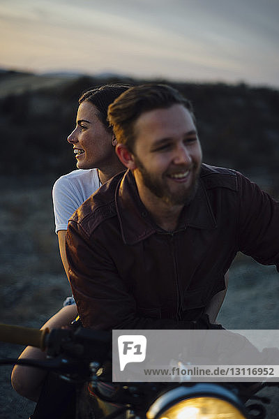 Happy couple sitting on motorcycle at field during sunset