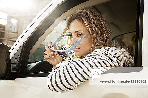 Nachdenkliche Frau hält Sonnenbrille  während sie im Auto sitzt