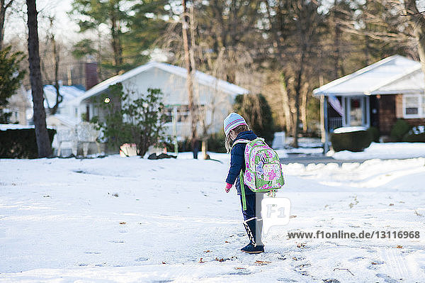 Girl carrying backpack walking on snowy field