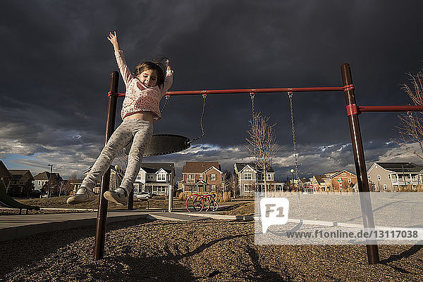 Verspieltes Mädchen springt auf dem Spielplatz von der Schaukel gegen stürmische Wolken