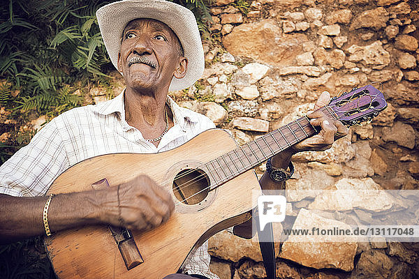 Mann spielt Gitarre  während er an einer Steinmauer sitzt