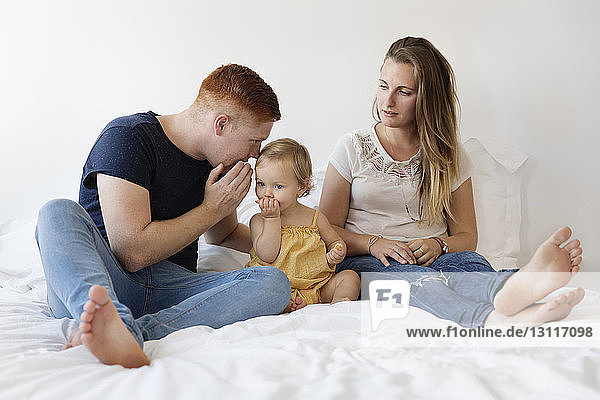 Parents with daughter sitting on bed at home