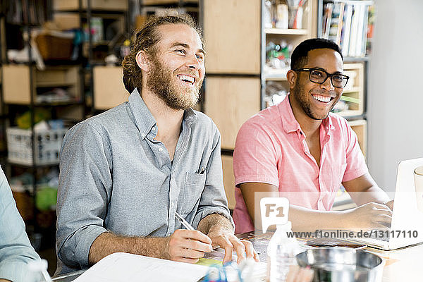 Happy businessmen looking away while sitting at conference table