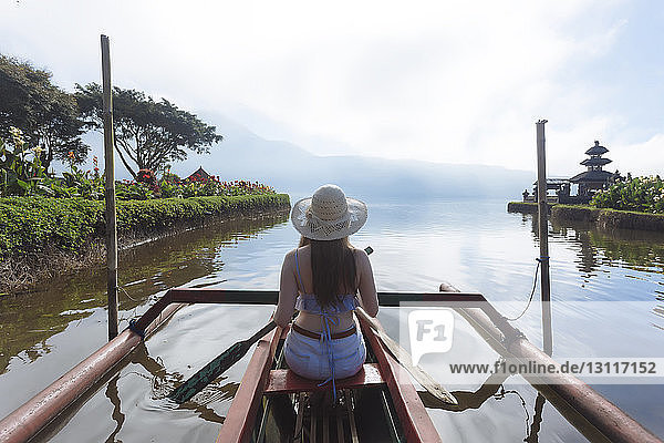 Rear view of woman sitting in boat on lake against cloudy sky
