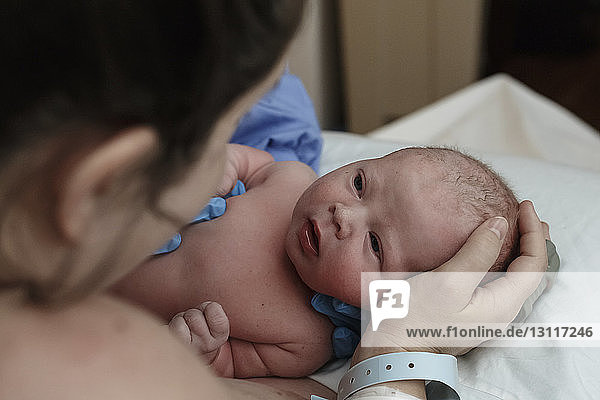 Shirtless newborn son looking at mother in hospital