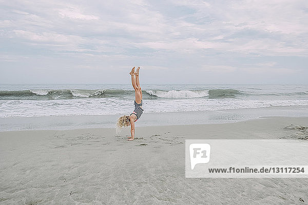 Full length of girl doing handstand at Cape May Beach against sea and sky