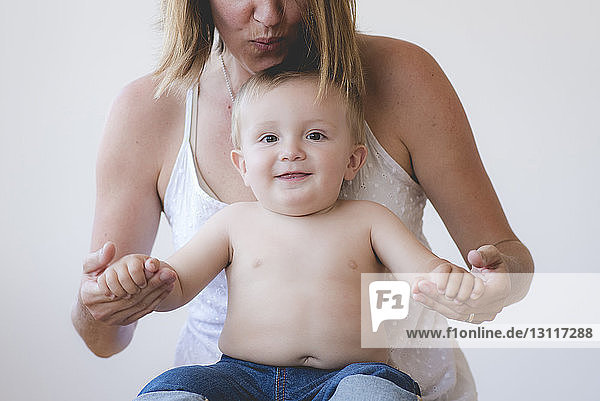 Portrait of cute shirtless son with mother against white background