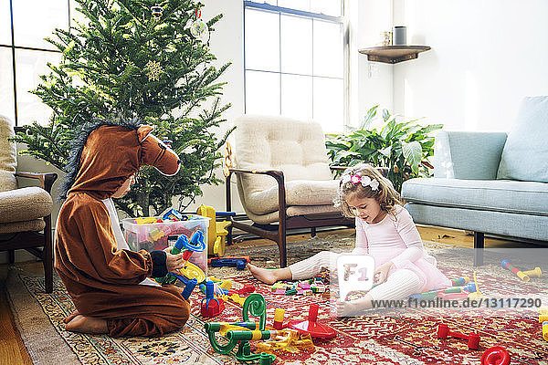 Geschwister spielen mit Bauklötzen  während sie zu Hause am Weihnachtsbaum sitzen