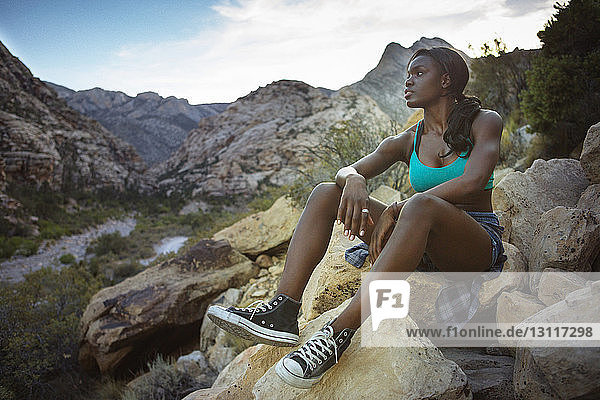 Nachdenkliche Frau sitzt auf Felsen gegen Berge