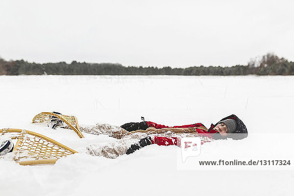 Teenage boy wearing snowshoes lying on snow covered field against sky