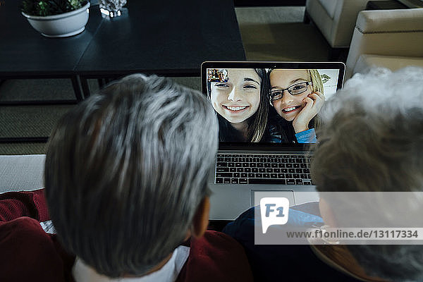 Hochwinkelansicht der Videokonferenz der Großeltern mit den Enkelinnen über Laptop-Computer zu Hause