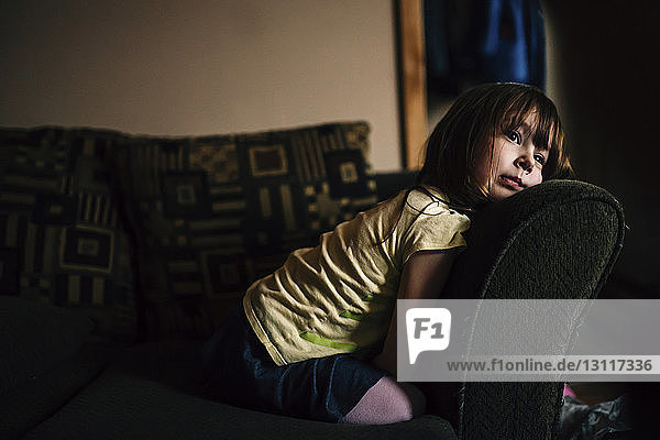 Gelangweiltes Mädchen schaut weg  während es auf dem Sofa kniet
