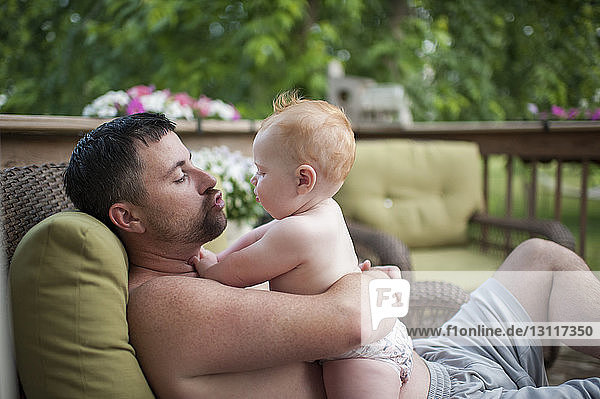 Shirtless father playing with son while relaxing on porch