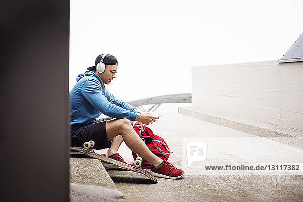 Mann hört Musik  während er auf einem Fußweg auf einem Parkplatz sitzt