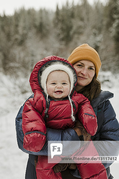 Portrait of mother carrying daughter while standing in forest during winter