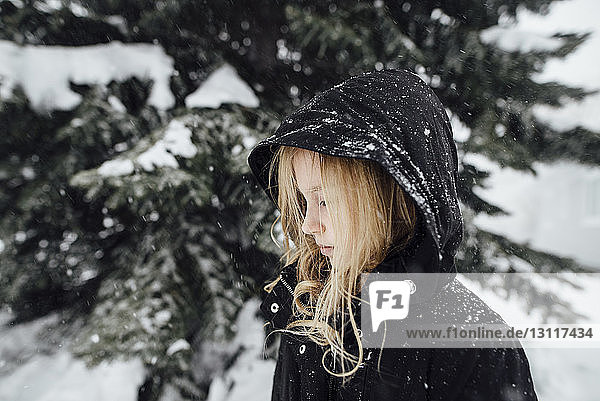 Seitenansicht eines Mädchens  das an einem schneebedeckten Baum im Hof steht