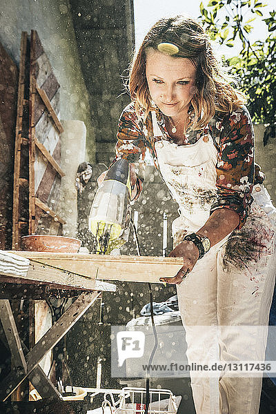 Künstlerin schneidet Holzbohlen bei der Arbeit im Hinterhof
