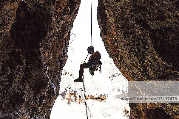 Wanderer hängt am Seil inmitten von Felsformationen in einer Höhle in der Wüste