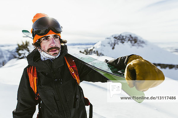 Wanderer trägt Ski auf Schulter gegen schneebedeckten Berg