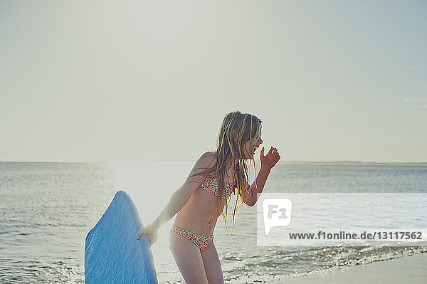 Fröhliches Mädchen hält Surfbrett am Strand gegen den Himmel