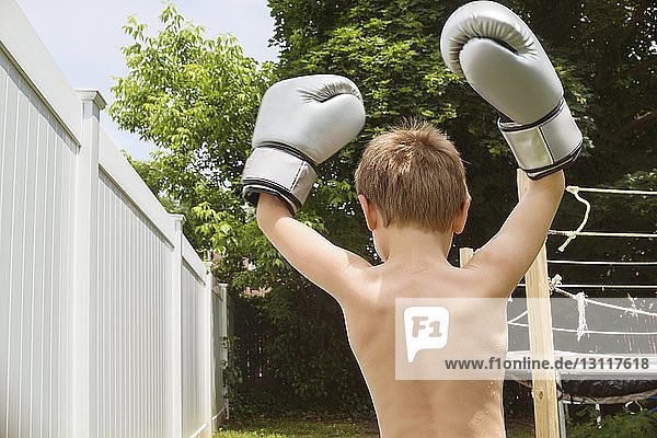 Rückansicht eines Jungen  der im Hinterhof die Arme hebt  während er Boxhandschuhe trägt